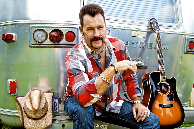 Country Music Artist photo Dean Young sitting on back of airstream trailer acoustic guitar and cowboy hat on bumper beside him