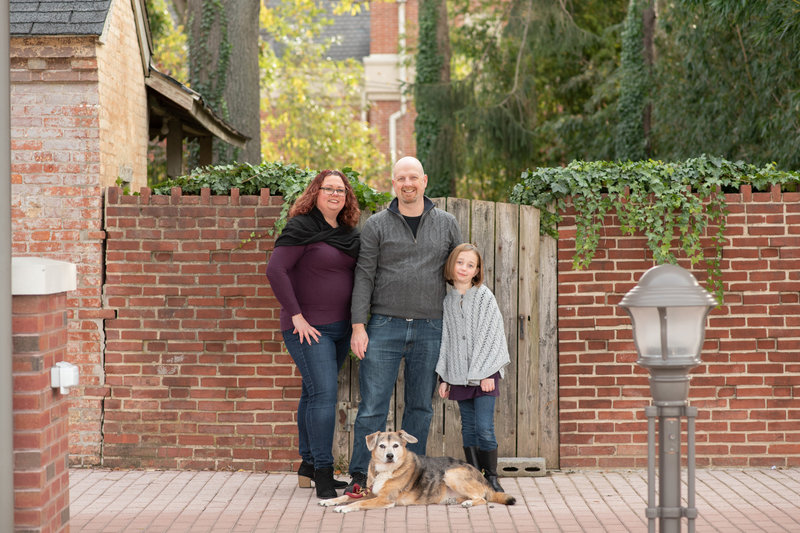 Family of three with their dog.. Street. Brick wall. gate