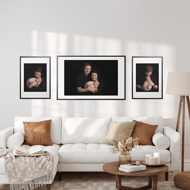 A family newborn session of framed artwork hangs above a couch in a living room.