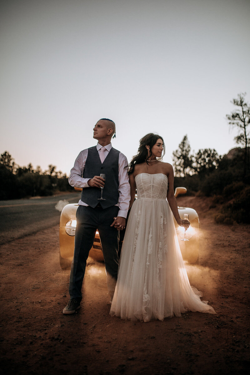 bride and groom with champagne getaway car wedding sedona lace boho dress grey suit