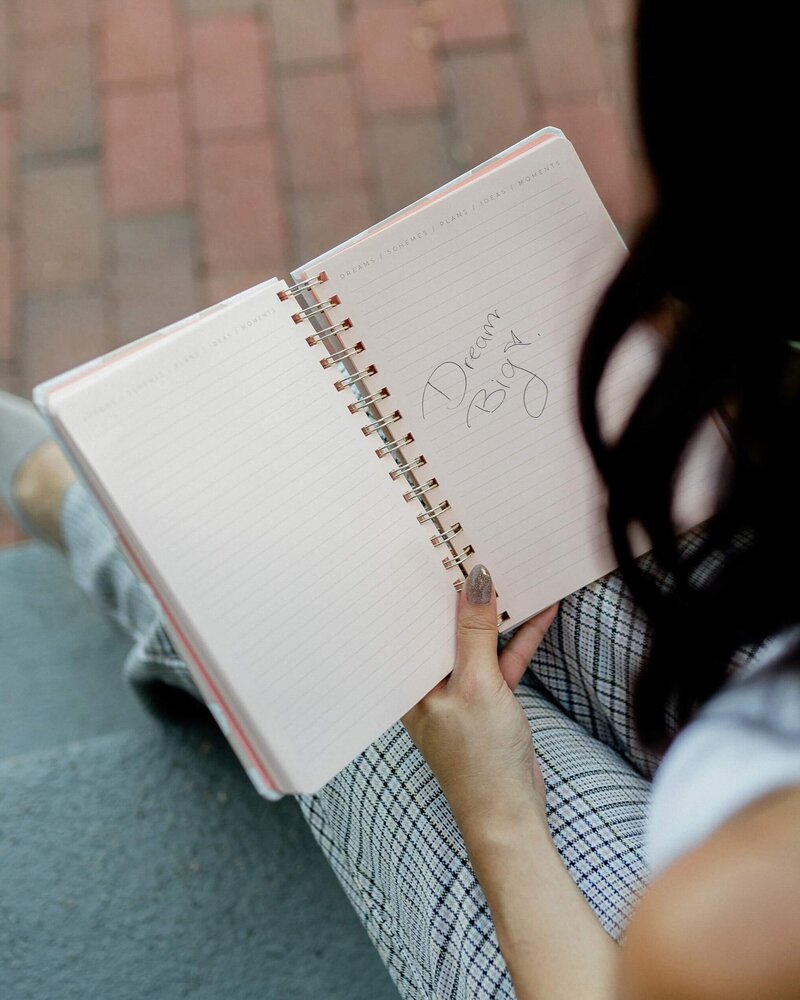 woman holding a notebook with a note that says "Dream Big"