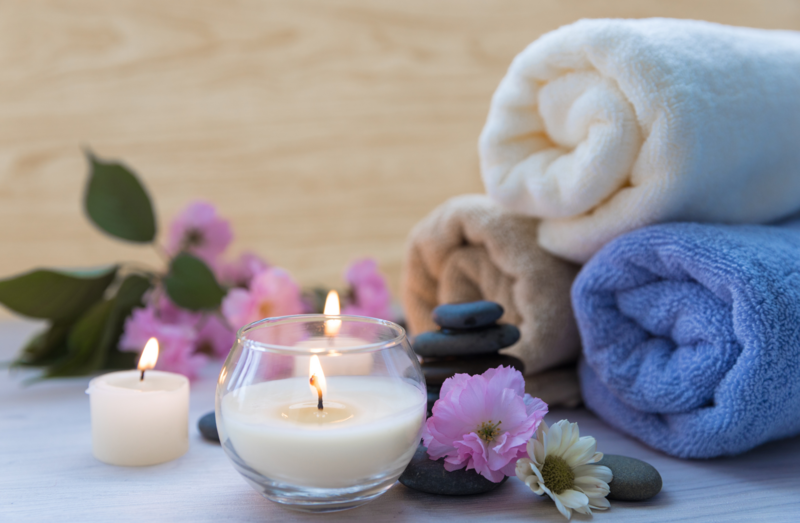 a lit candle with flowers, spa stones, and spa towels in the background.