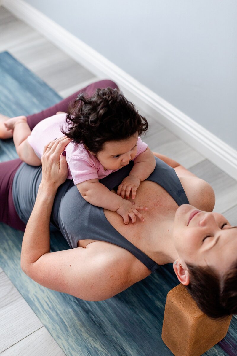 female yoga instructor lays with baby on her chest for mommy and me class in LA