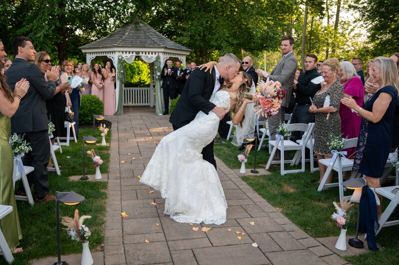 New England outdoor wedding ceremony with the bride and groom sharing a dip kiss while guests celebrate.