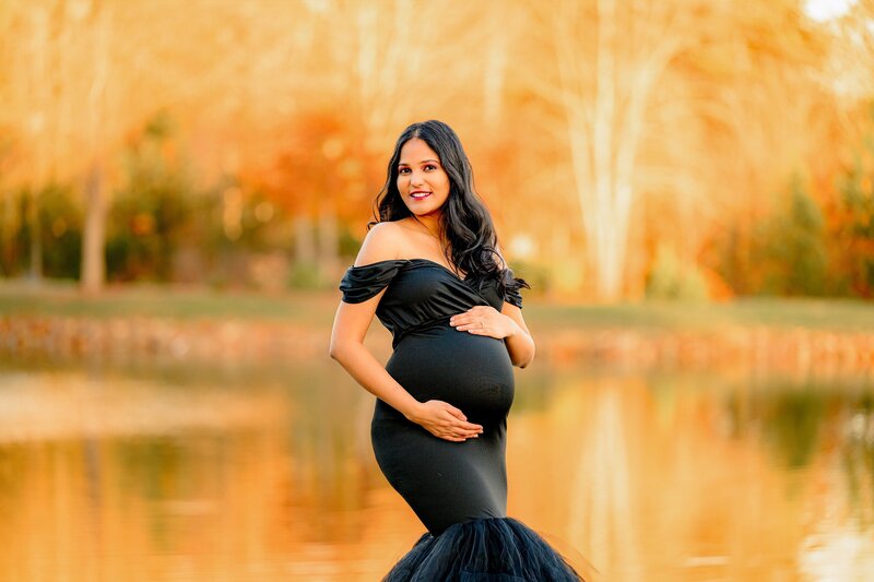 Charlotte Area mother dressed in a glamorous black dress that's off the shoulder with both hands on her belly during her maternity photos