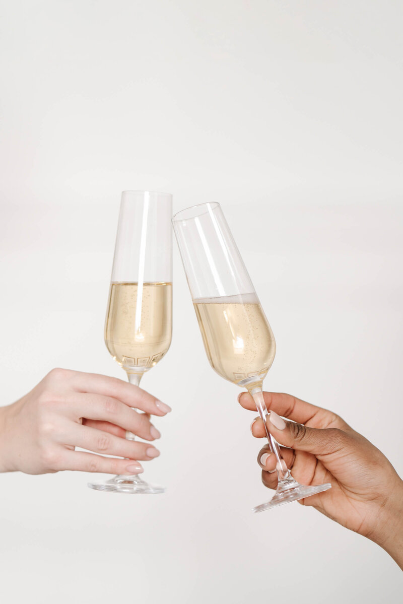 Women holding a glass of champagne doing a cheers by Haute Stock
