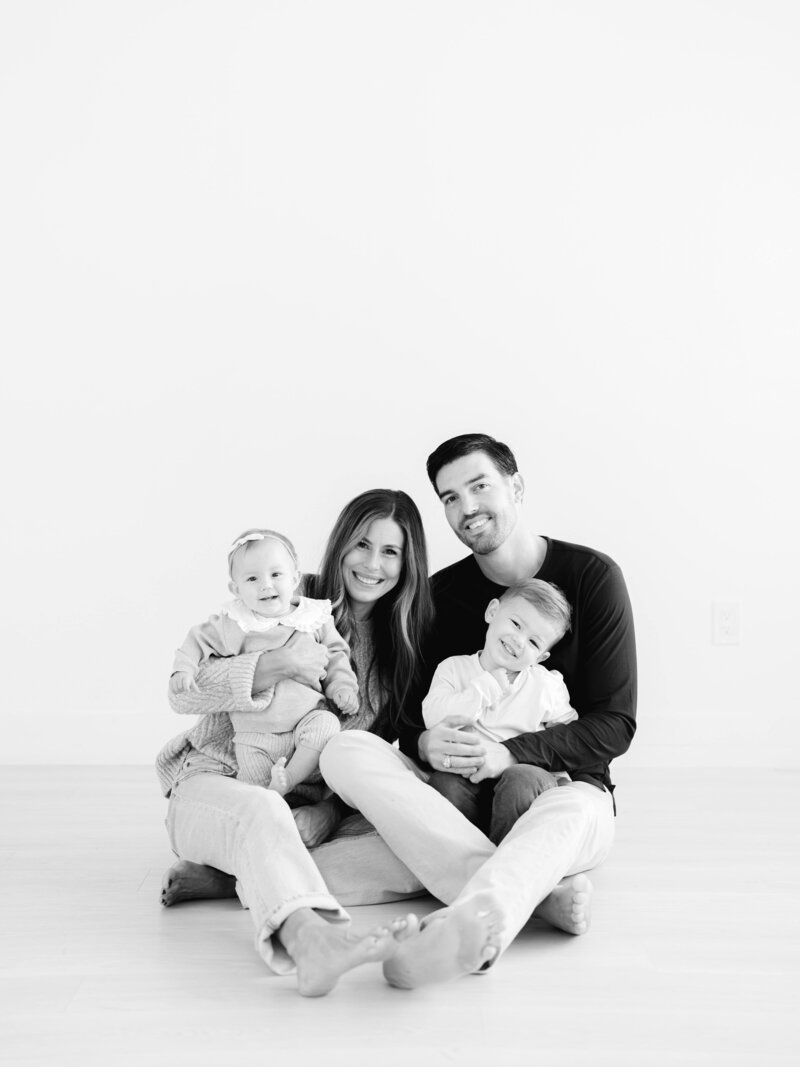 Smiling family with mom and dad with two young children sitting in a studio floor