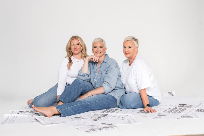 Amy, Kristina and Rachel in white and denim clothing, sitting on the floor which is covered in newspapers