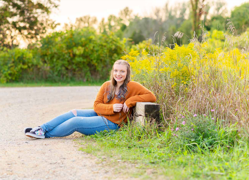 high school senior girl sitting against wood plank with yellow flowers in backdrop
