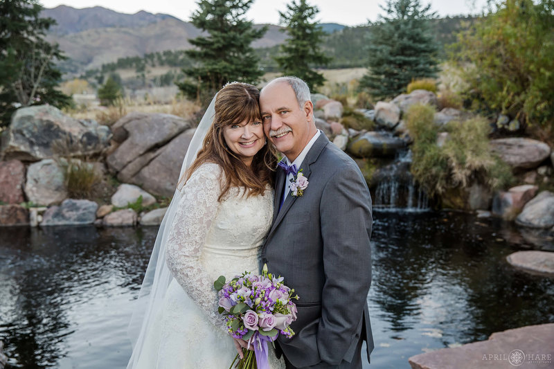 Couple poses for a portrait in front of pretty pond with mini waterfall at The Greenbriar Inn Boulder CO