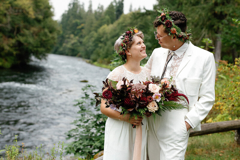 Couple wearing flower crowns looking at each other in front of river