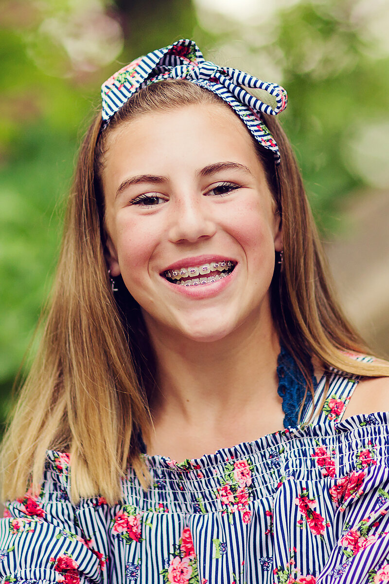 Nice portrait of a tween in a colorful striped shirt with flowers on it, matching bow, smiling big with her braces.