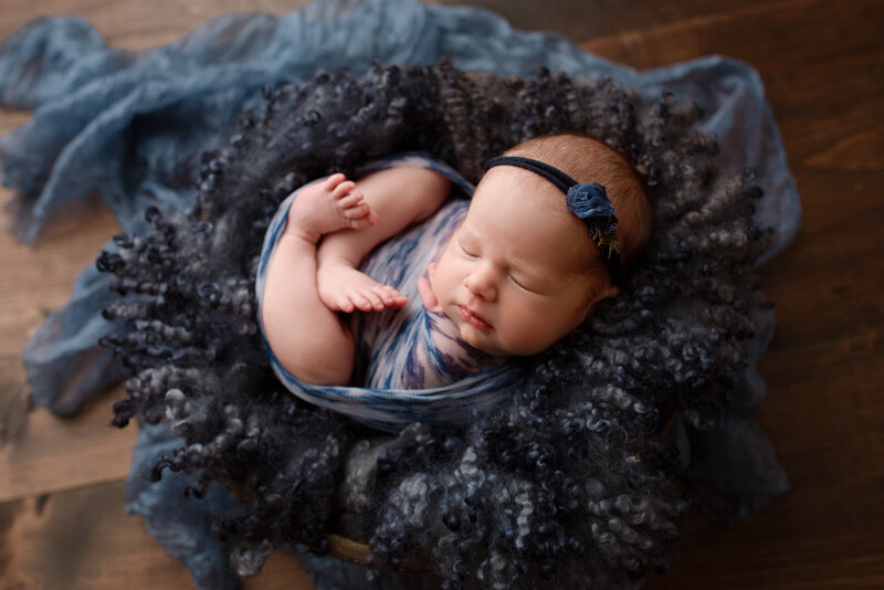 baby girl posing on a navy blue flokati and wrapped in a blue wrap