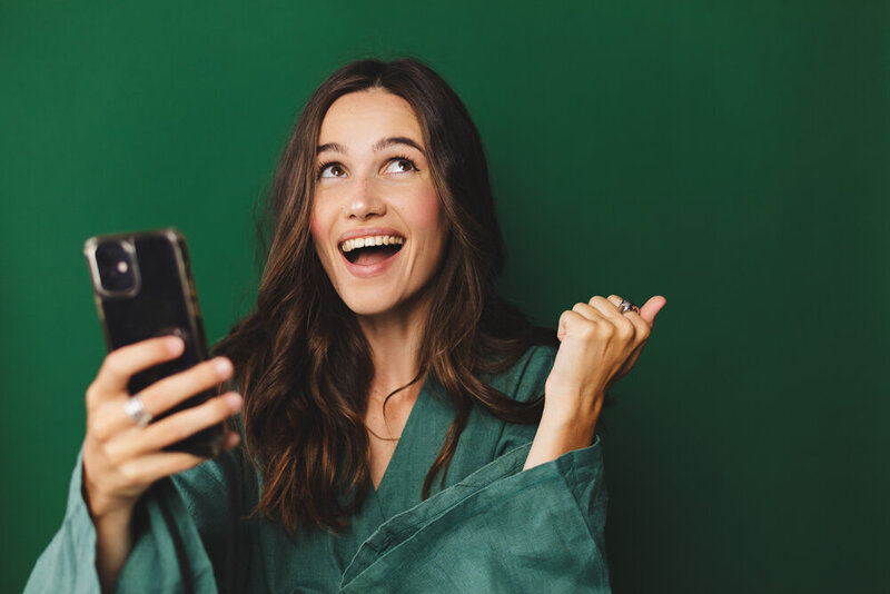 Young business woman looking up and smiling while holding a cellphone  in one hand and raising the other hand making a fist