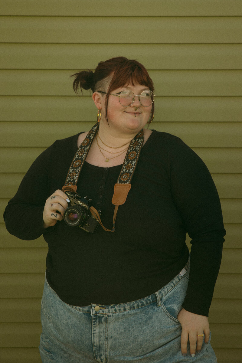 A photographer holds her camera in a snowy forest, smiling at her equipment