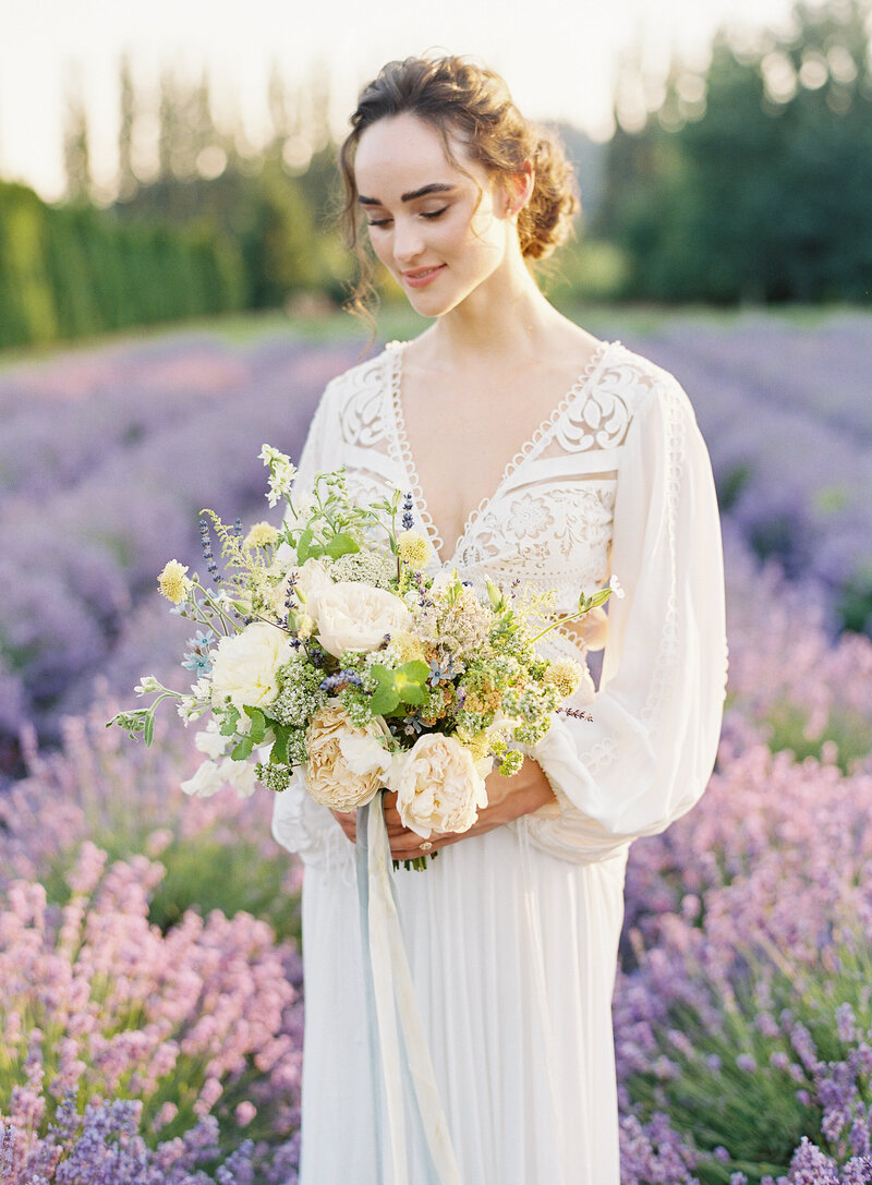 Photo of a bride at sunset in a purple lavender field in Washington wearing a billowy boho wedding dress holding a whimsical pastel floral bouquet