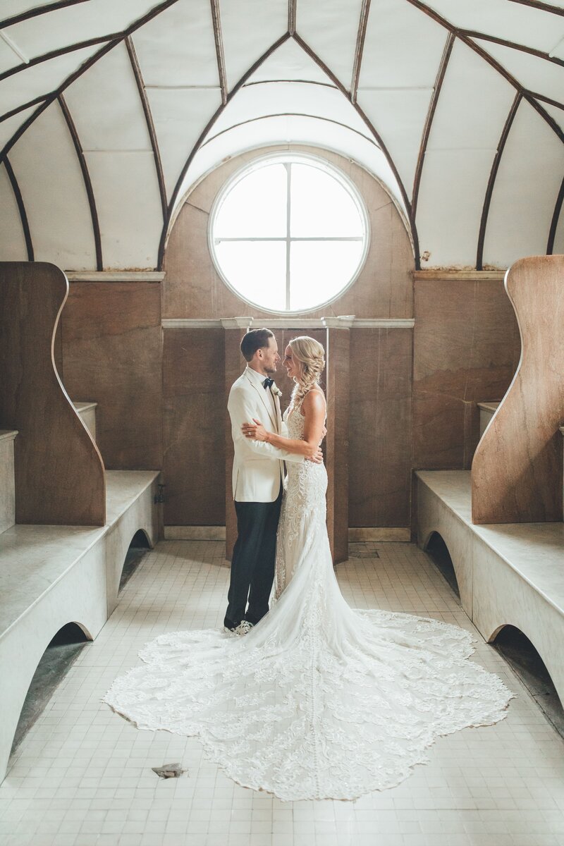 A Bride and Groom smiling at each other below a circular window inside a Treasury Venue