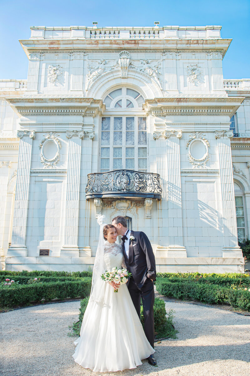 Groom kissing bride's cheek in front of The Rosecliff