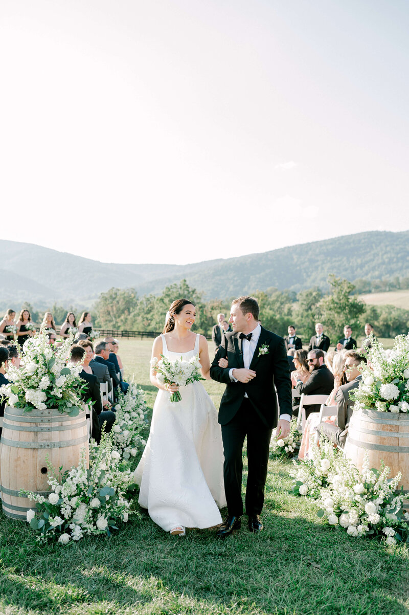 Classy Bride and Groom recessing up a white floral aisle at the picturesque venue, Kings Family Vineyard in Charlottesville, Virginia.