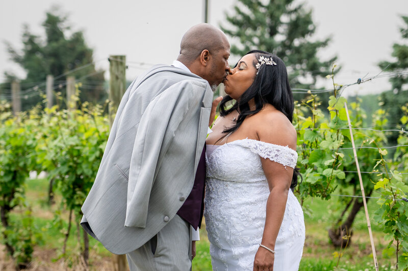Bride and groom sharing a kiss between vineyard rows surrounded by leafy vines – photographed by wedding photographer Niko Coric – Lumen Clarity Media