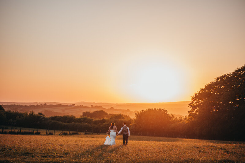 bride and groom holding hands walking into sunset