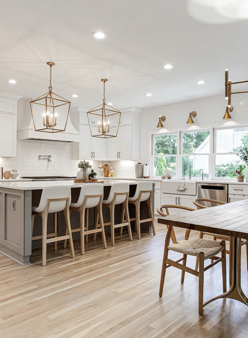 Bright, modern kitchen with white cabinets, gold light fixtures, a large island with bar stools, and a wooden dining table with chairs.