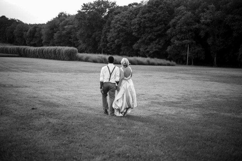 Bride and groom walk through a field at Betsy's Barn