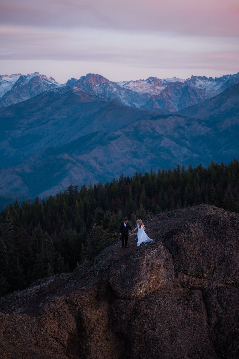 Bride and groom holding hands after hiking up to a lookout with mountain views in Washington State on their elopement day