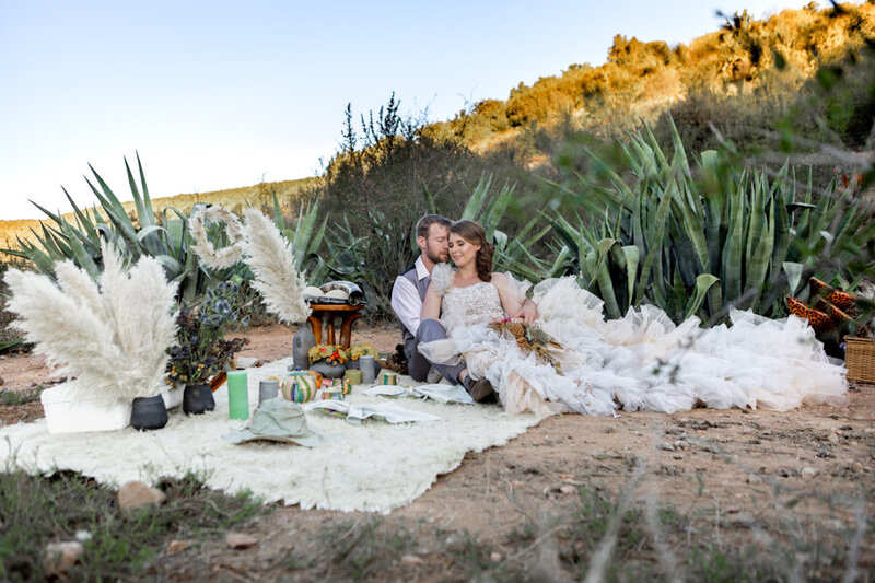 bride and groom snuggled in desert greenery next to a picnic