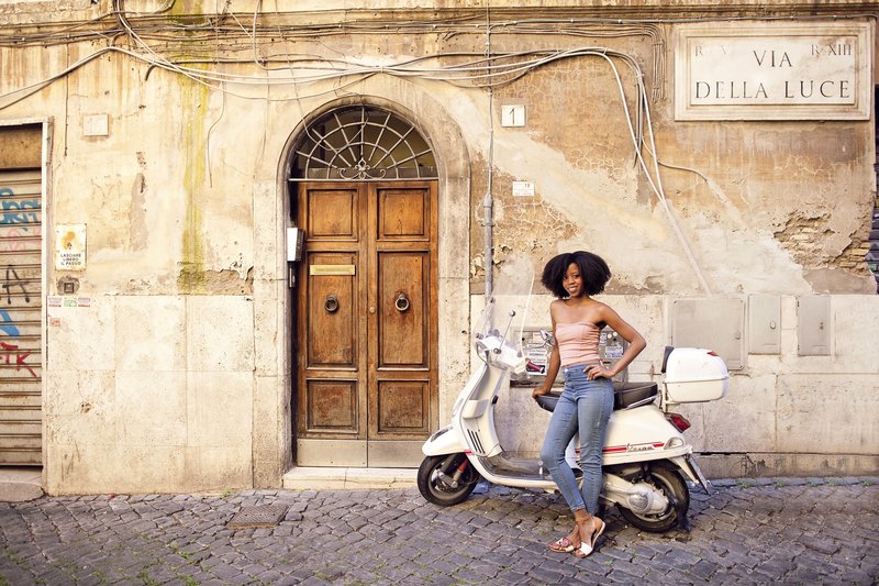 A beautiful girl in front classic roman building with wooden door and white vespa motorino. Taken by Rome Solo Travel Photographer, Tricia Anne Photography