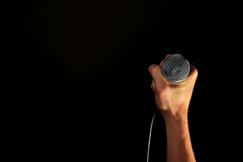 single hand holding a condencer mic against a black backdrop 