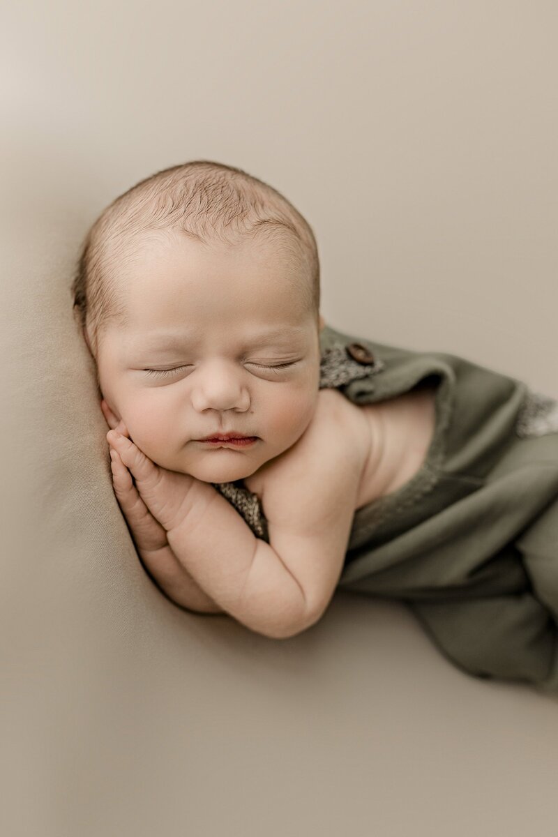 Close up image of a baby boy laying on his side with his hands underneath his cheek during his Studio newborn session