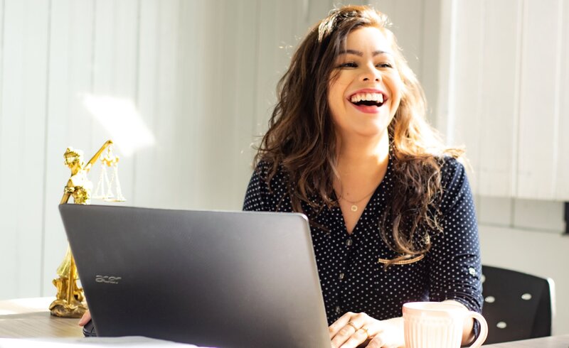 Photo of a young woman laughing and sitting in front of laptop
