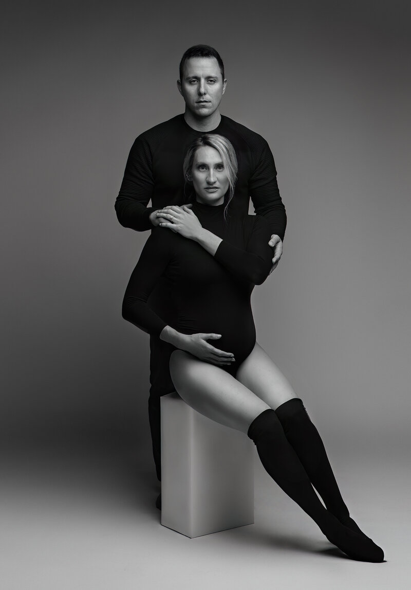 Black and white maternity portrait of expectant couple in minimalist studio, posed in sculptural lighting at Tamara Hudson Studios