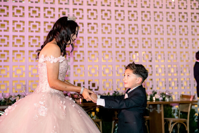 In front of the Hart and  Main breezeblock wall, the birthday girl dances with her young brother during her Quincenera