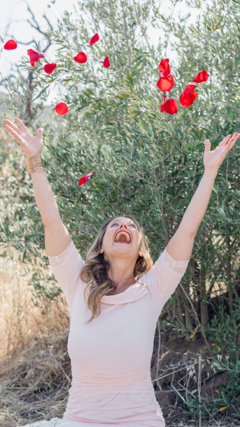 Keri Nola throwing roses petals in the air on a blanket in a grassy field