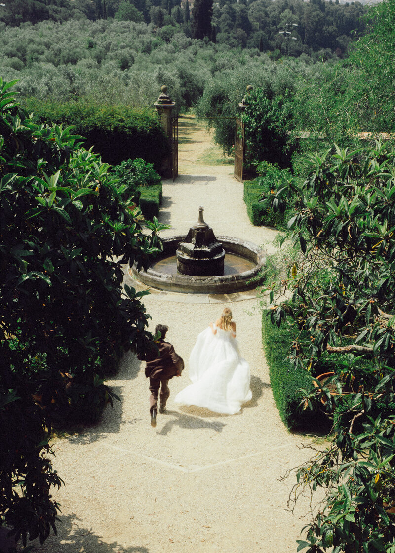 Bride and groom walking through a sunlit Italian garden, captured in a romantic, cinematic style by a luxury destination wedding photographer UK with film-inspired tones.