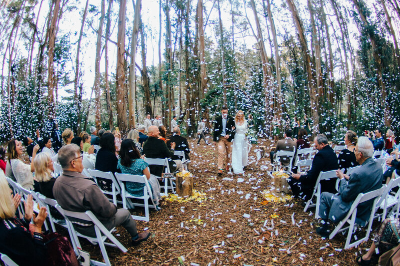 Bride and groom walk back down the aisle after taking vows with confetti in the air