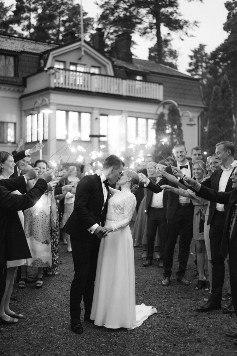 Documentary wedding photo of bride and groom and guests with sparkles in front of Airisniemi manor in Turku. A cheerful and romantic image by wedding photographer Hannika Gabrielsson.