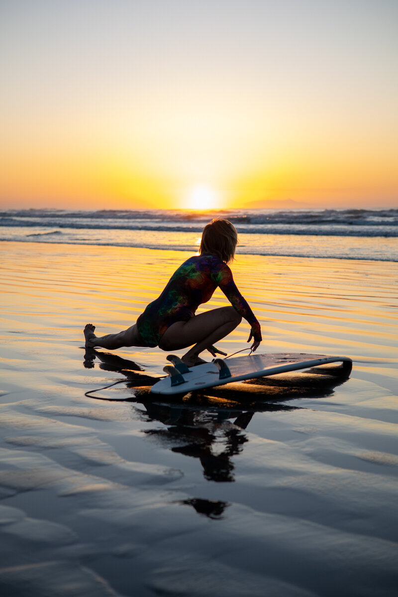 Surfer does yoga on beach during sunrise