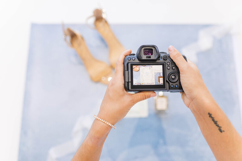 A photo of nashville wedding photographer, Brooke Elliott's hands holding a camera with a wedding day flat lat in the background.