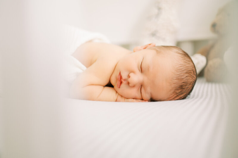 Newborn baby boy sleeps in his belly in white crib during in-home newborn session
