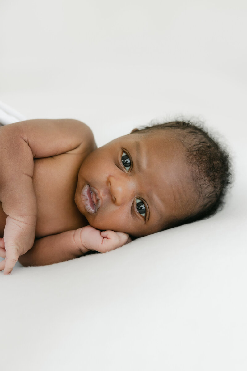 Newborn baby boy lays on his side and looks at the camera during newborn photography session
