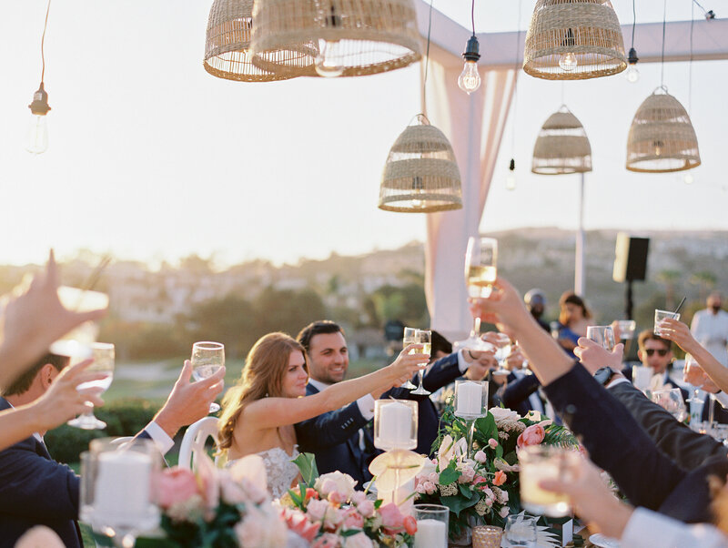 during reception couple and guests are cheering during sunset with lanterns hanging bove and twinkle lights