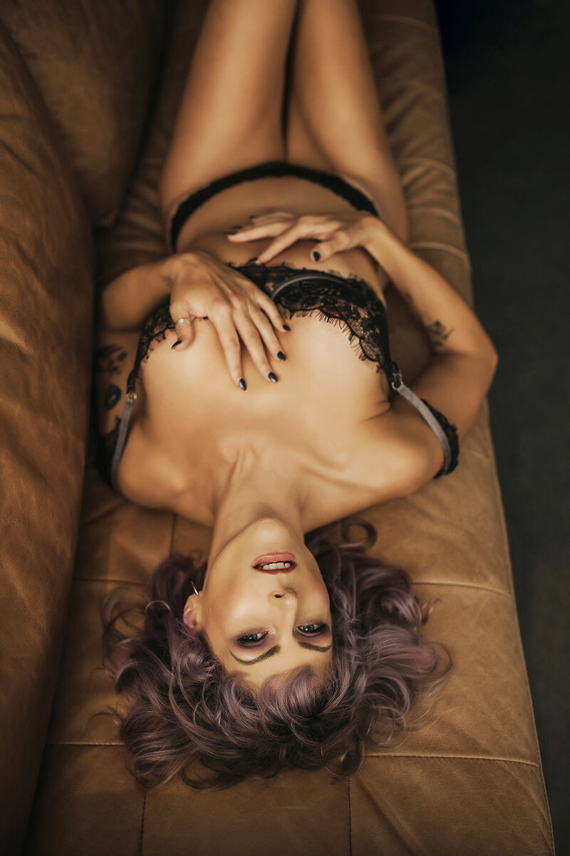 woman with purple hair posing on leather couch in boudoir studio