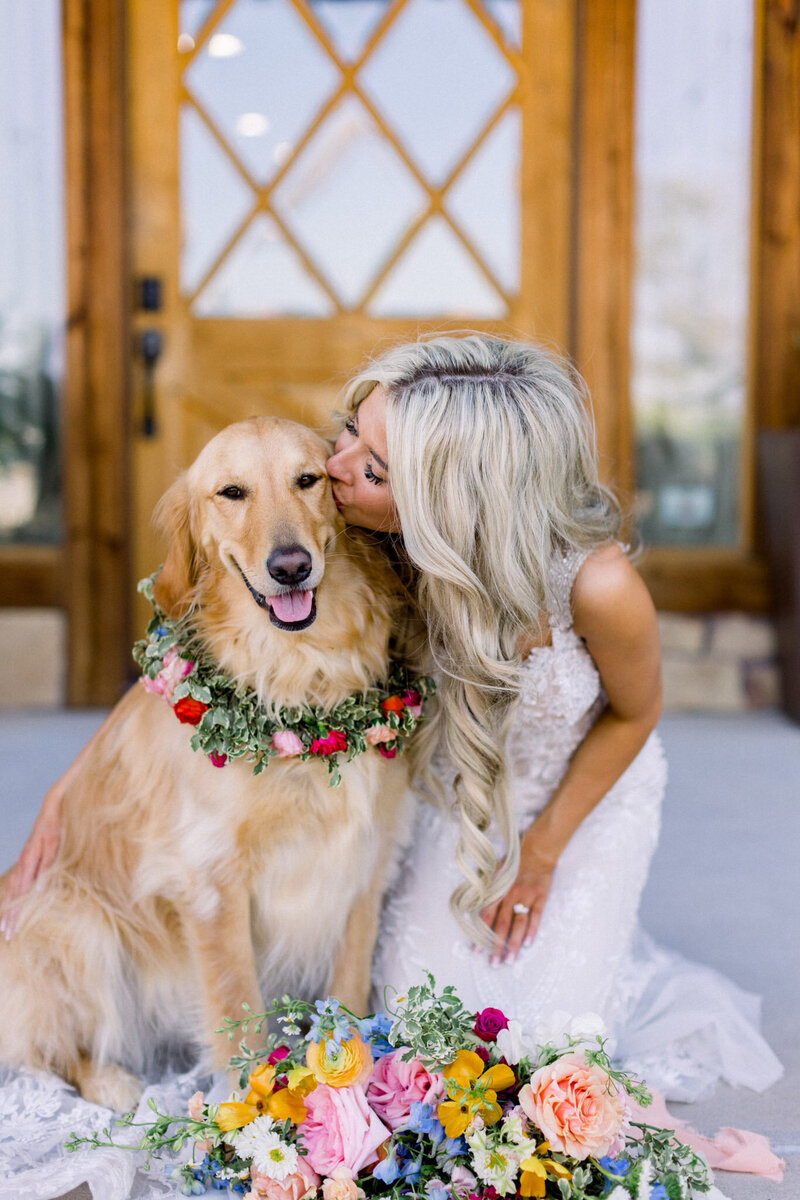 bride kissing her dog that has a flower collar on