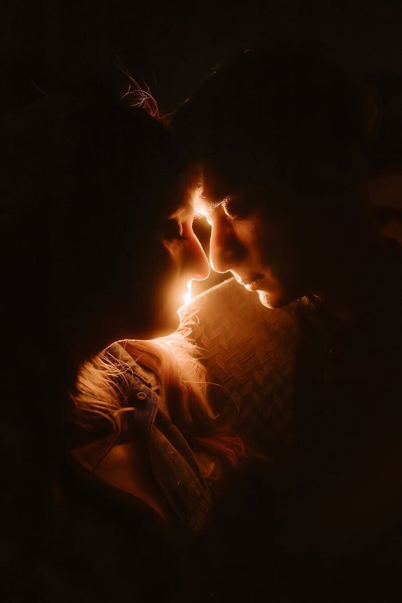 Close-up of a couple touching foreheads in the dark, their faces softly lit by a warm glow between them.