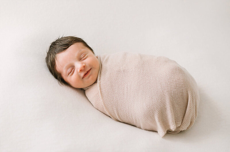 A newborn baby girl wrapped in a pink swaddles smiles in her sleep