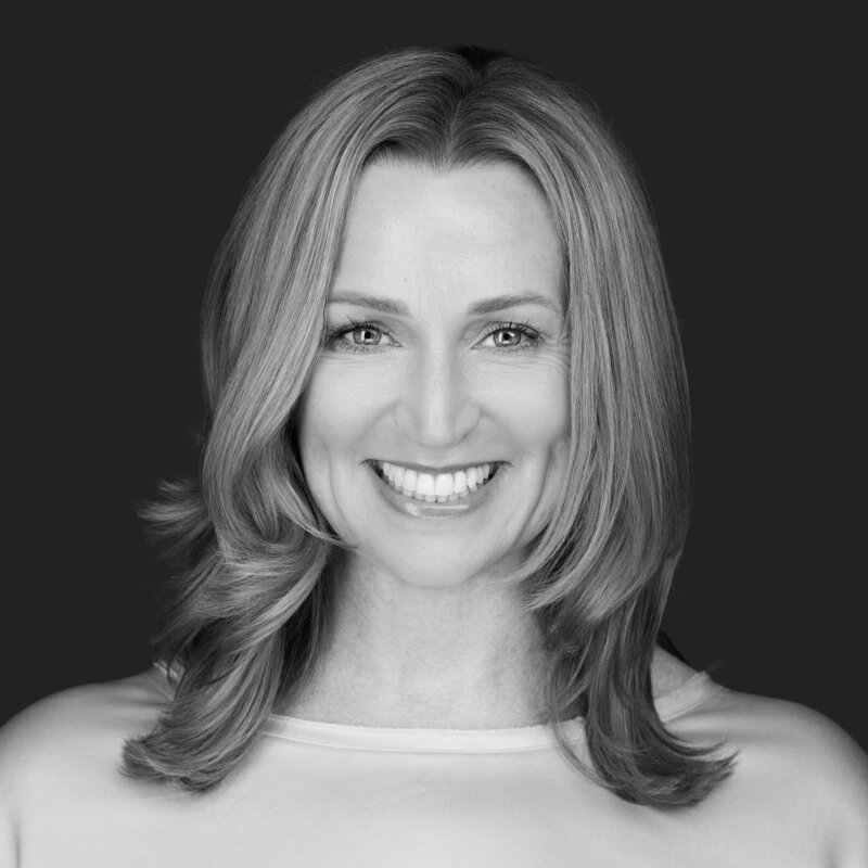 Jenn Cloutier professional headshot in black and white with bright smile, shoulder-length light hair, wearing light-colored top against dark background.