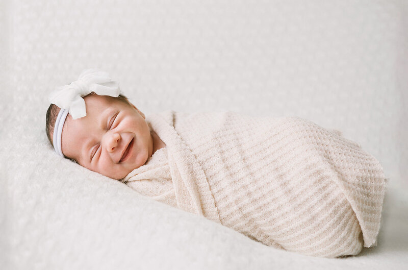 A newborn baby girl with a white bow headband smiling